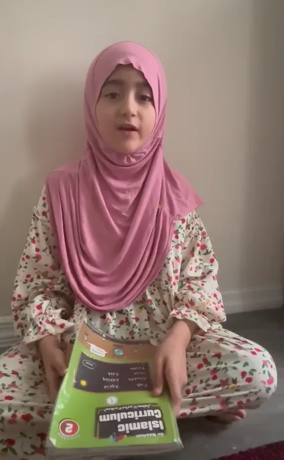 OQLS student in a pink hijab holding her Islamic studies book